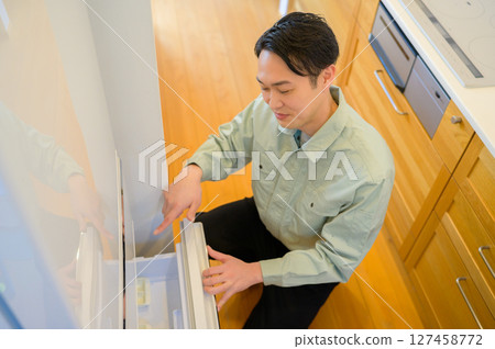 Japanese man in work clothes inspecting a refrigerator Japanese man in work clothes inspecting a refrigerator 127458772