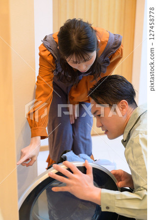 A Japanese man inspecting a washing machine and a woman watching over him 127458778
