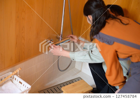 A Japanese man inspecting the water facilities in the bathroom and a woman watching over him A Japanese man inspecting the water facilities in the bathroom and a woman watching over him 127458784