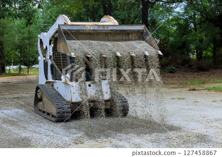 Heavy machinery spreads gravel on construction site in wooded area during preparation land improvement Heavy machinery spreads gravel on construction site in wooded area during preparation land improvement 127458867