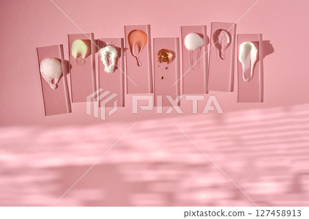 Samples of multi-colored cosmetic products on a pink background. 127458913