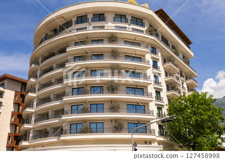 Modern apartment building with curved balconies and potted trees. Contemporary architecture, urban greenery, and residential luxury. 127458998