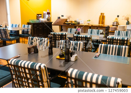 Modern hotel breakfast room with striped chairs and buffet area. Cozy interior, buffet service, and contemporary hospitality design. Modern hotel breakfast room with striped chairs and buffet area. Cozy interior, buffet service, and contemporary hospitality design. 127459003