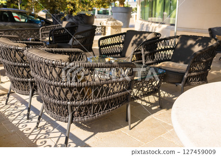 Outdoor wicker chairs with cushions in sunny cafe terrace. Modern outdoor seating, cozy atmosphere, and leisure lifestyle. 127459009