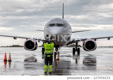 Airplane marshalling at the aiport apron in rainy weather. Passenger plane meeting Airplane marshalling at the aiport apron in rainy weather. Passenger plane meeting 127459153