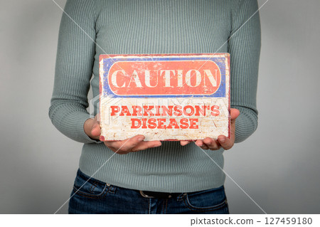 PARKINSON'S DISEASE. Caution Sign Held by Person in Casual Clothing 127459180