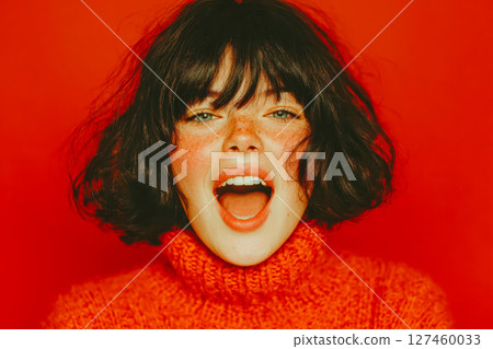 Young woman with short hair wearing bright sweater expressing joy against a vibrant background 127460033