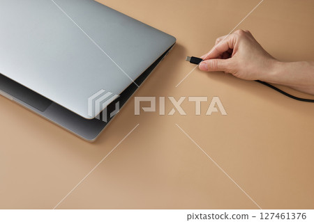 female hand plugging battery charger on laptop at beige table, closeup female hand plugging battery charger on laptop at beige table, closeup 127461376