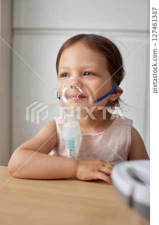 cute little toddler girl inhaling medicine on nebulizer and holding it on her own 127461387