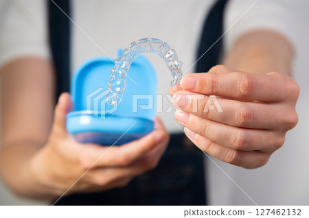 Hands of a young Caucasian woman holding transparent dental aligners and a case for storing them. Plastic braces with space copy 127462132