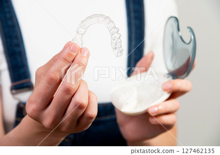 Hands of a young Caucasian woman holding transparent dental aligners and a case for storing them. Plastic braces with space copy 127462135