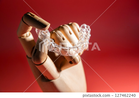 Teeth alignment trays on pink background in wooden fake hand. Modern teeth alignment, technology, billboard or website advertising layout Teeth alignment trays on pink background in wooden fake hand. Modern teeth alignment, technology, billboard or website advertising layout 127462240