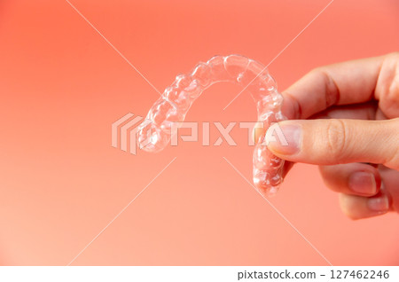 Hand hold invisible aligners plastic braces dentistry retainers to straighten teeth temporary removable straightener with plastic dentures on light peach background 127462246