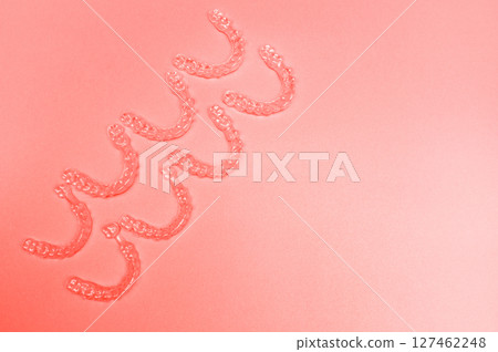 Invisible teeth retainers lie on a bright pink background. Close-up of a modern way to straighten teeth 127462248