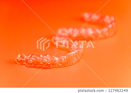 Invisible teeth retainers lie on a bright orange background. Close-up of a modern way to straighten teeth 127462249