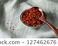 Bowl of crushed red pepper flakes with a wooden spoon on green linen fabric 127462676