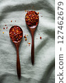Two wooden spoons filled with crushed red chili flakes on a soft green fabric background 127462679