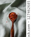 Wooden spoon filled with crushed red chili flakes on green fabric background 127462685