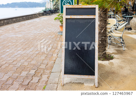 Wooden frame chalkboard stands on summer pavement. The concept shows outdoor signage, seasonal business, and blank advertising opportunity. Copy space. Wooden frame chalkboard stands on summer pavement. The concept shows outdoor signage, seasonal business, and blank advertising opportunity. Copy space. 127463967