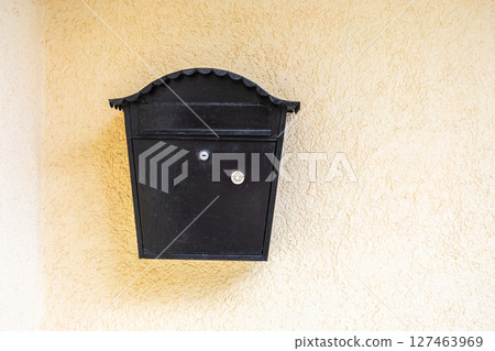 Black mailbox on bright white wall. Postal service, communication symbol, and street detail in sunny environment. Copy space Black mailbox on bright white wall. Postal service, communication symbol, and street detail in sunny environment. Copy space 127463969