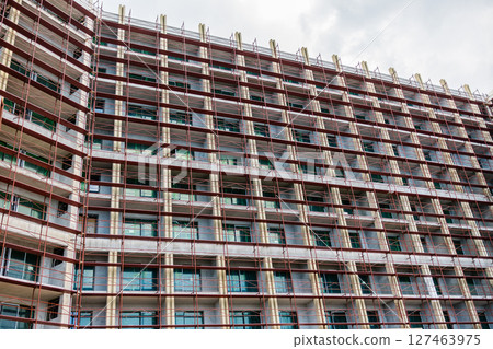 Modern glass building under construction with full scaffolding. Urban development, contemporary architecture, and city infrastructure progress. 127463975