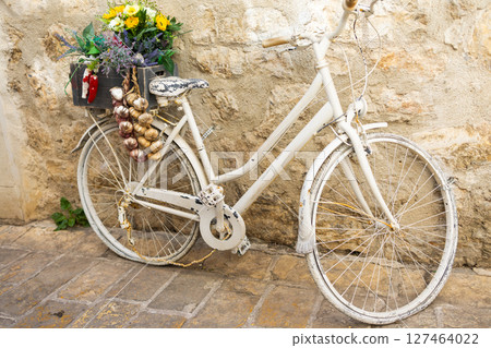 Decorative white bicycle with garlic, flowers. Vintage charm, street decor, and restaurant marketing. Decorative white bicycle with garlic, flowers. Vintage charm, street decor, and restaurant marketing. 127464022