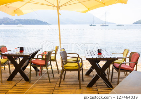 Outdoor cafe or restaurant with sea view and empty chairs. Coastal relaxation, summer tourism, and beachfront dining in the Mediterranean region. Outdoor cafe or restaurant with sea view and empty chairs. Coastal relaxation, summer tourism, and beachfront dining in the Mediterranean region. 127464039