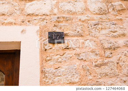 Number 17 plaque on rustic stone wall near wooden doorway. Summer travel, architectural heritage, and identification in old European towns. Number 17 plaque on rustic stone wall near wooden doorway. Summer travel, architectural heritage, and identification in old European towns. 127464068