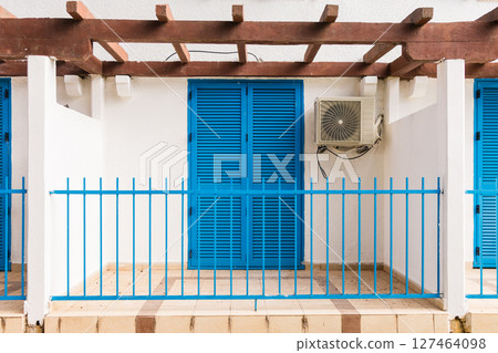 Mediterranean house with blue shutters behind pine trees. Relaxation, seaside living, and Mediterranean charm in a peaceful green environment. 127464098