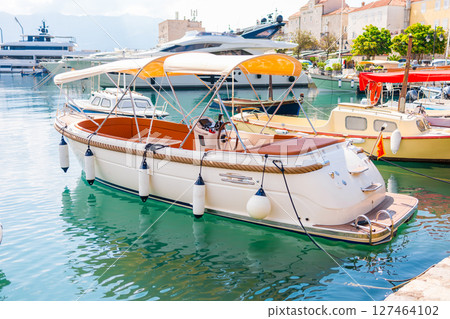 Small boats floating in marina with mountain backdrop. Coastal lifestyle, nautical tourism, and scenic summer destination. 127464102
