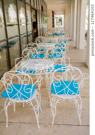 White patio chairs with blue cushions in sunny veranda. Outdoor elegance, Mediterranean leisure, and summer hospitality design. 127464103