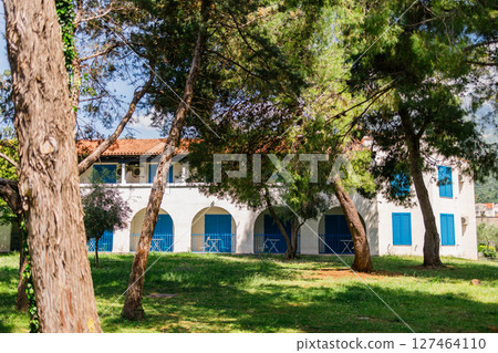Mediterranean house with blue shutters behind pine trees. Relaxation, seaside living, and Mediterranean charm in a peaceful green environment. Mediterranean house with blue shutters behind pine trees. Relaxation, seaside living, and Mediterranean charm in a peaceful green environment. 127464110