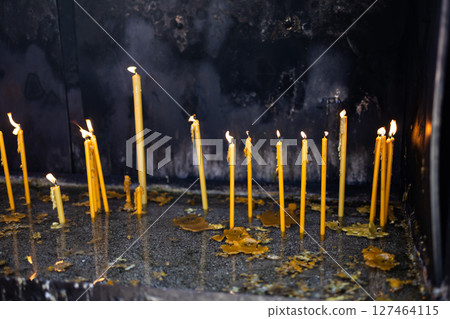 Lit candles in sand inside a church shrine. Spiritual ritual, personal prayer, and the quiet power of remembrance and sacred tradition. 127464115