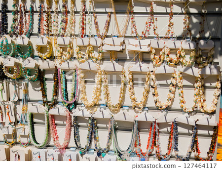 Colorful necklaces made of shells and gemstones on market display. Beach fashion, handmade souvenirs, and traditional crafts for tourists in coastal destinations. Colorful necklaces made of shells and gemstones on market display. Beach fashion, handmade souvenirs, and traditional crafts for tourists in coastal destinations. 127464117