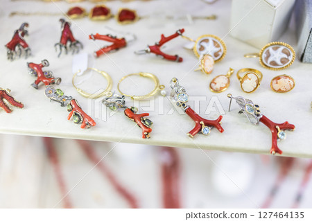 Red coral jewelry display in artisan shop. Handcrafted accessories, marine motifs, and Mediterranean design influence local fashion and cultural aesthetics. Red coral jewelry display in artisan shop. Handcrafted accessories, marine motifs, and Mediterranean design influence local fashion and cultural aesthetics. 127464135