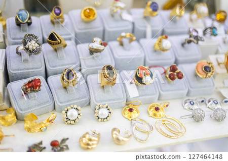 Colorful gemstone rings and vintage earrings displayed on soft velvet stands. Jewelry craftsmanship, luxury shopping, and retro elegance in boutique markets. 127464148