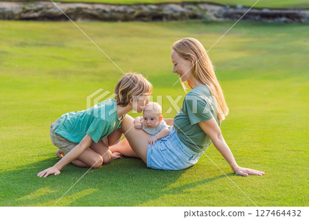 Mother, older son, and newborn baby on a meadow in the park. Family spending quality time together in nature. Parenthood, love, and family bond concept 127464432