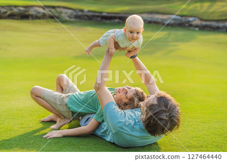 Father, older son, and newborn baby on a meadow in the park. Family spending quality time together in nature. Parenthood, love, and family bond concept Father, older son, and newborn baby on a meadow in the park. Family spending quality time together in nature. Parenthood, love, and family bond concept 127464440