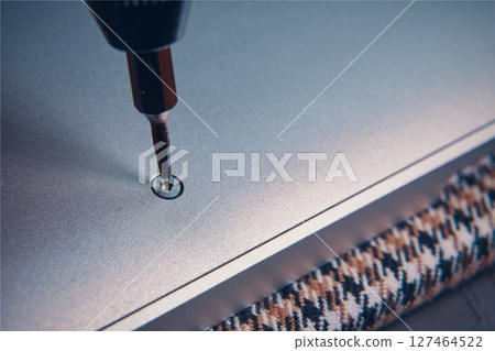 A close-up view of a screwdriver inserting a screw into a metallic surface, showcasing precision work. A close-up view of a screwdriver inserting a screw into a metallic surface, showcasing precision work. 127464522