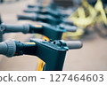 A row of electric scooters lined up on the street, showcasing their sleek metal frames and electric blue accents. The Bicycle handlebars and engineering design indicate a modern Machine construction 127464603