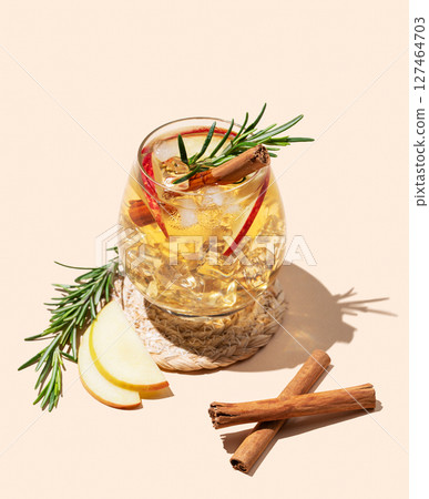 Apple cocktail or cider in a glass with ice, cinnamon and rosemary on a beige background 127464703