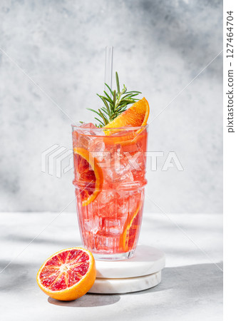 Blood orange cocktail with ice and rosemary on a marble stand on a gray background with shadows 127464704