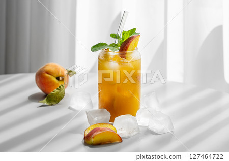 Refreshing peach cocktail, lemonade or iced tea on a white table near window with shadows Refreshing peach cocktail, lemonade or iced tea on a white table near window with shadows 127464722