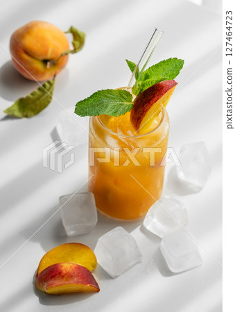 Refreshing peach cocktail, lemonade or iced tea on a white table with shadows, ice cubes and fruits. 127464723