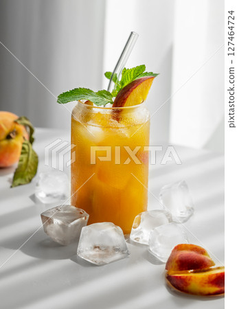 Refreshing peach cocktail, lemonade or iced tea on a white table near window with shadows 127464724