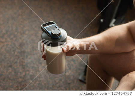 Close up shot of bottle with holding protein shaker in mans hand at gym. Bodybuilder during strength training. Fitness healthy lifestyle concept. Supplement product, creatine, glutamine for workout. Close up shot of bottle with holding protein shaker in mans hand at gym. Bodybuilder during strength training. Fitness healthy lifestyle concept. Supplement product, creatine, glutamine for workout. 127464797