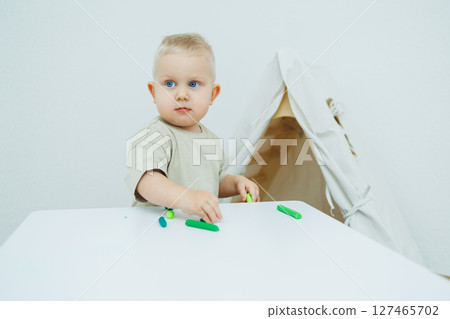A little one-year-old boy is sculpting plasticine while standing at the table. The child is playing with educational toys. A little one-year-old boy is sculpting plasticine while standing at the table. The child is playing with educational toys. 127465702