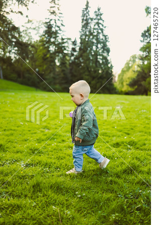 Cute boy running on the grass in a stylish shirt and sunbathing in the sun. Carefree childhood with joyful laughter of a child. Toddler having fun and enjoying a walk in nature. 127465720
