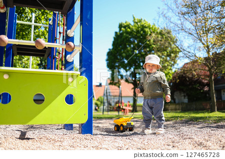 Toddler boy playing on the playground outside with his plastic car. Cute 2 year old boy playing with a car in the yard. Child walking outdoors. 127465728