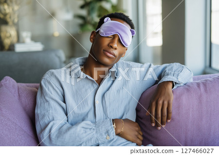 A man wearing a purple eye mask is sitting on a couch 127466027